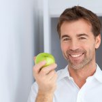 man smiling and holding an apple