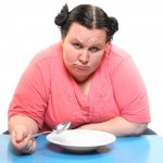 Overweight woman is sad over an empty plate